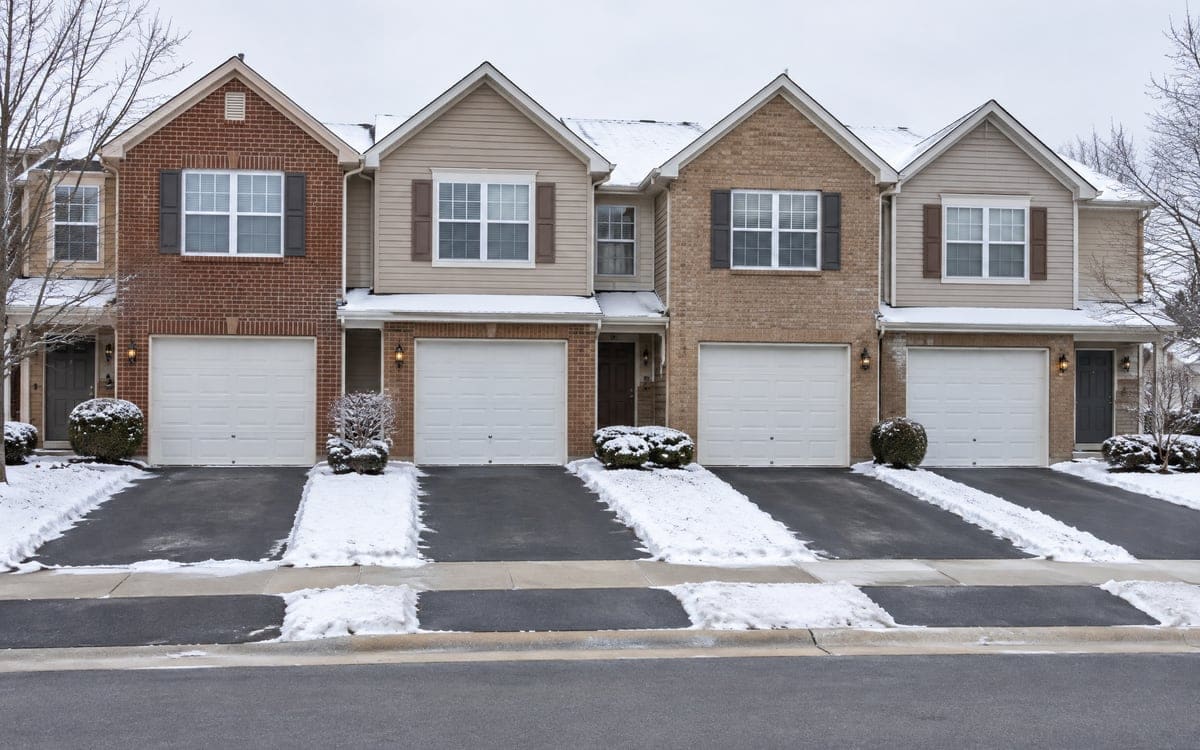 A row of attached homes with matching single garage doors under light snow.