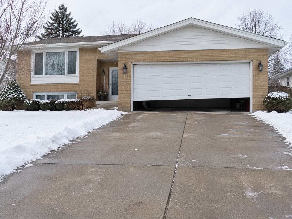 Emergency garage door repair for a white two-car door stuck partway open and uneven over a snowy driveway.