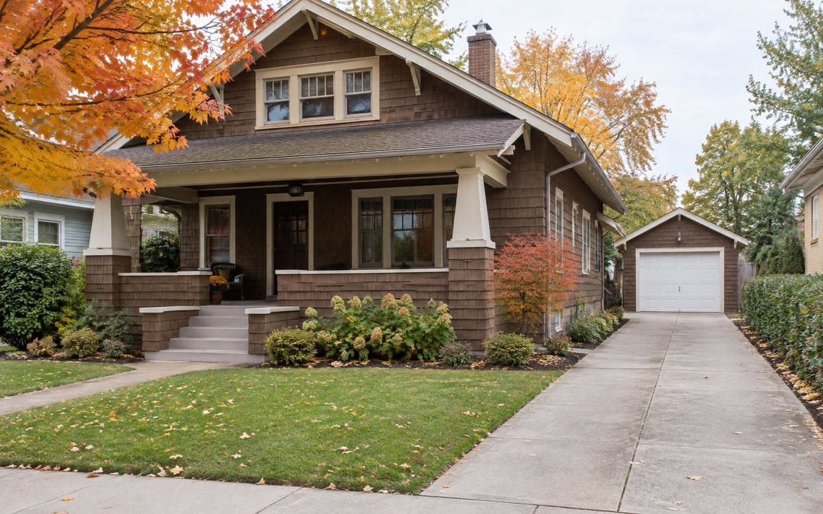 Older home garage door repair: a white wood door on a detached garage behind a shingled Craftsman bungalow.