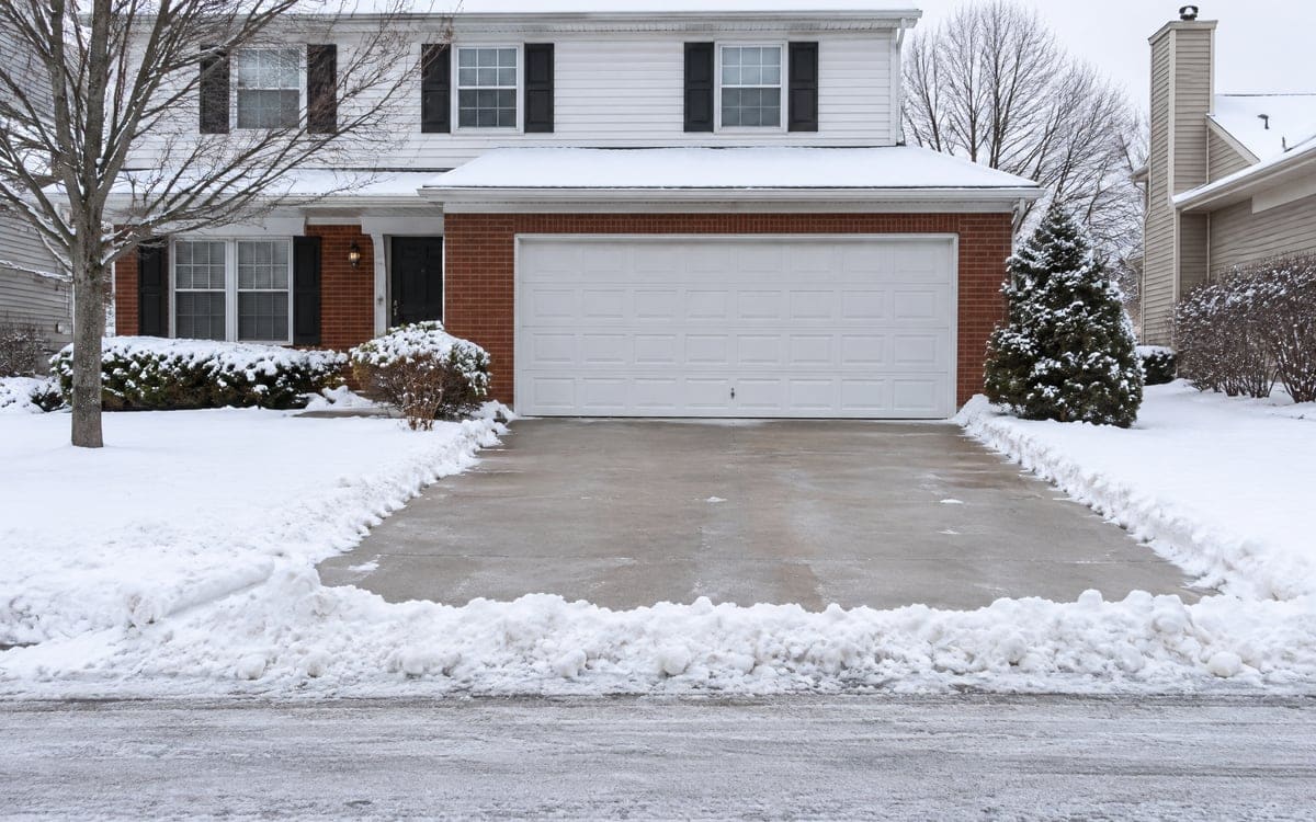 A plowed snow ridge across a driveway below a white two-car door, winter wear that leads to garage door repair.