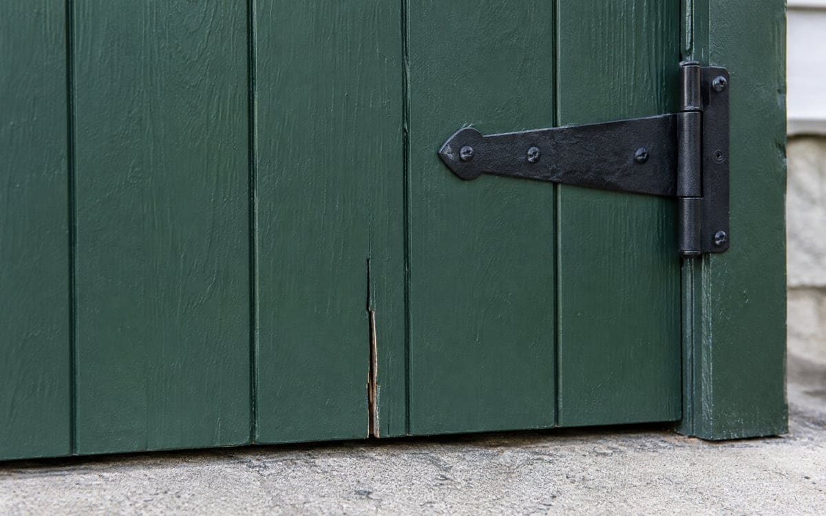 A split board at the bottom of a painted wood garage door, a case for garage door panel replacement or repair.