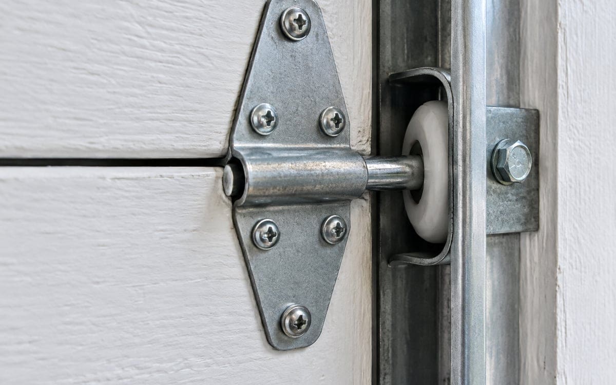 Garage door roller repair: a roller riding in its track, held by a hinge on the edge of a door section.